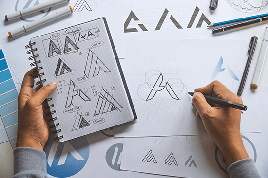 Eine Person erstellt verschiedene Logokonzepte auf einem Blatt Papier